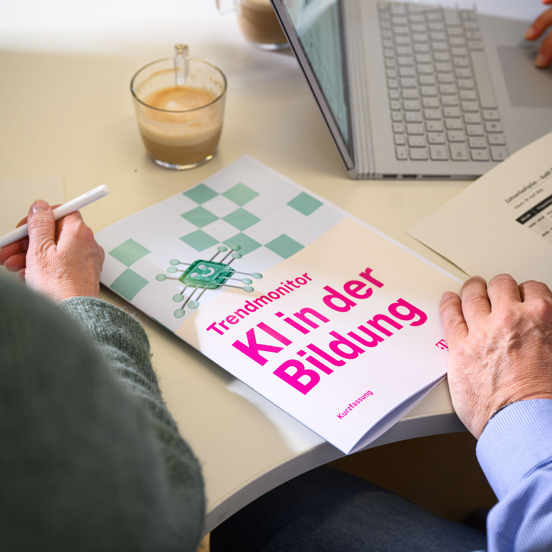 Der "Trendmonitor KI in der Bildung" liegt auf einem Schreibtisch. Eine Hand blättert.