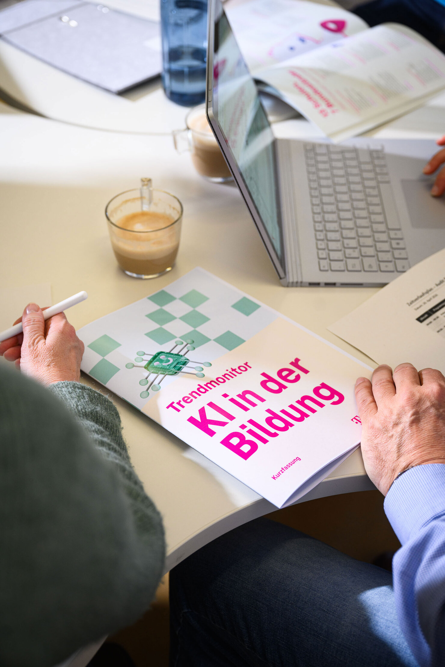 Der "Trendmonitor KI in der Bildung" liegt auf einem Schreibtisch. Eine Hand blättert.