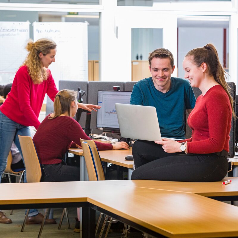 Drei Erwachsene arbeiten gemeinsam auf einer Bürofläche.