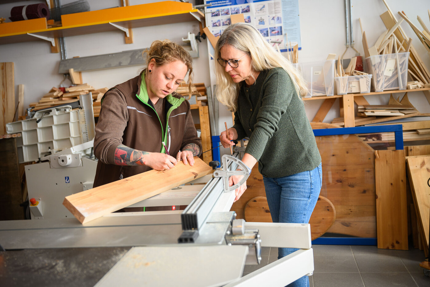 Zwei Frauen arbeiten gemeinsam mit einer Säge in einem Werkstattraum.