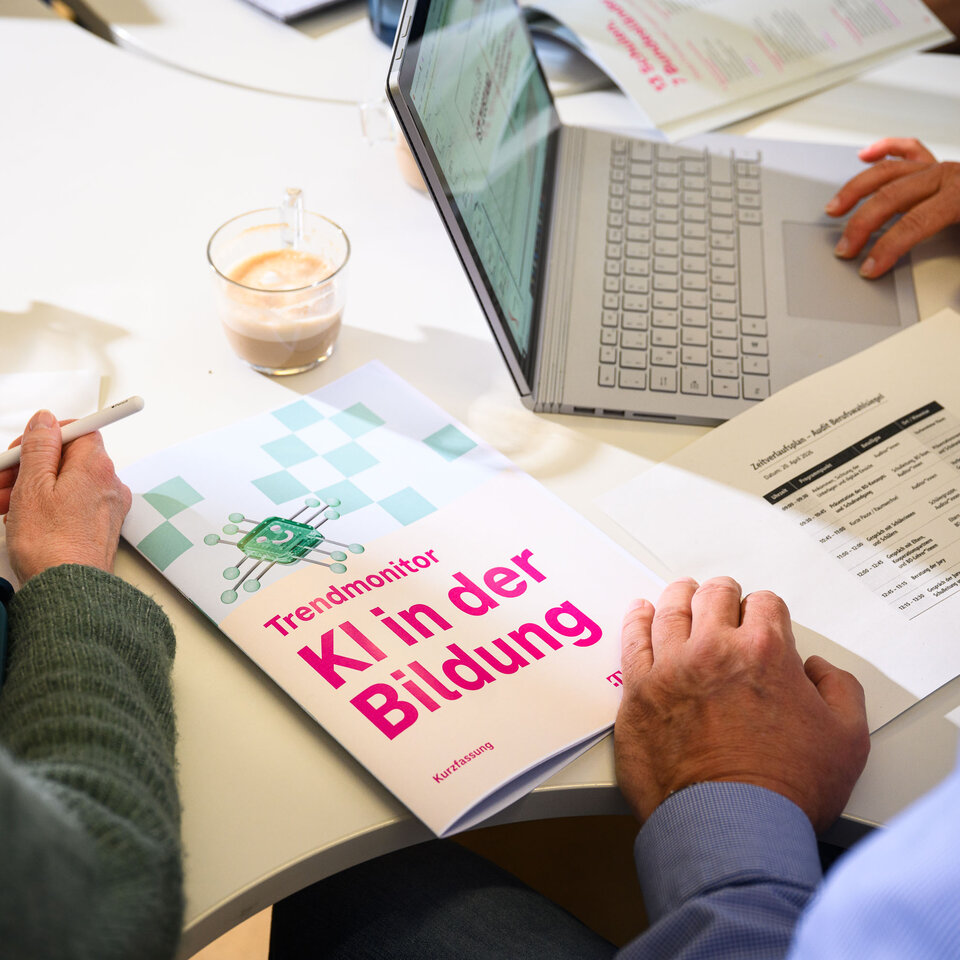 Der "Trendmonitor KI in der Bildung" liegt auf einem Schreibtisch. Eine Hand blättert.