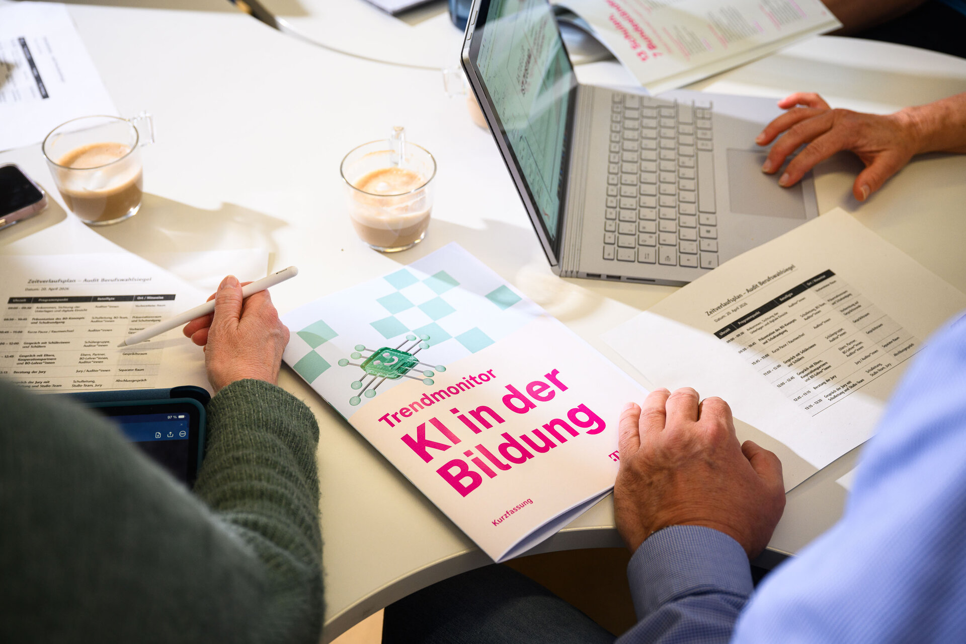 Der "Trendmonitor KI in der Bildung" liegt auf einem Schreibtisch. Eine Hand blättert.