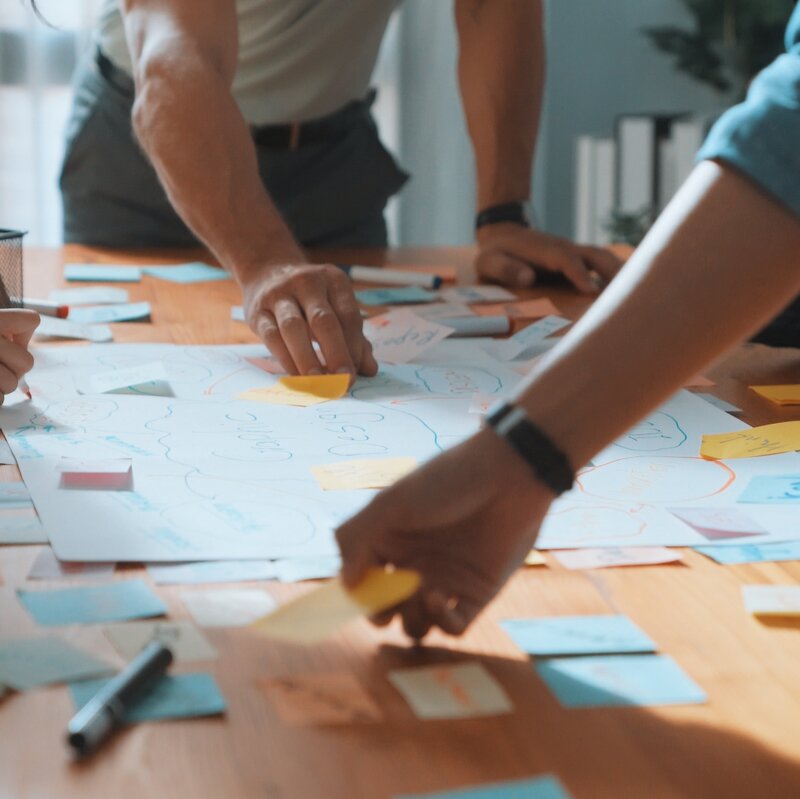 Hände arbeiten gemeinsam auf einem Tisch und sortieren Klebezettelchen.