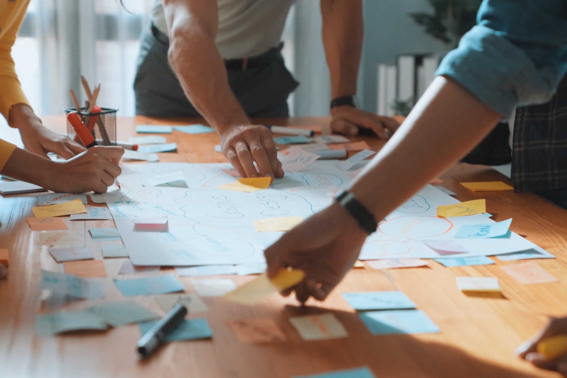 Hände arbeiten gemeinsam auf einem Tisch und sortieren Klebezettelchen.