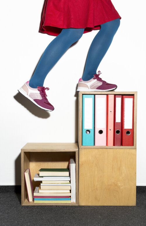 Eine Frau läuft aufeinandergestellte Regale hoch, die Ordner enthalten.