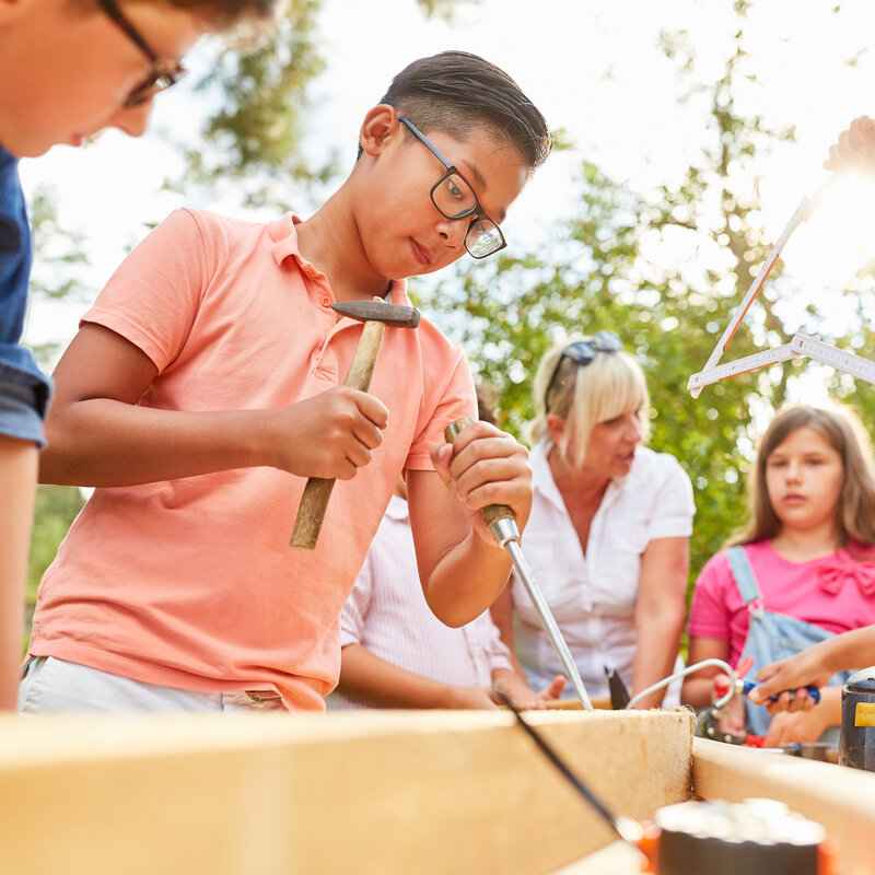 Kinder arbeiten gemeinsam draußen an einer Werkbank.