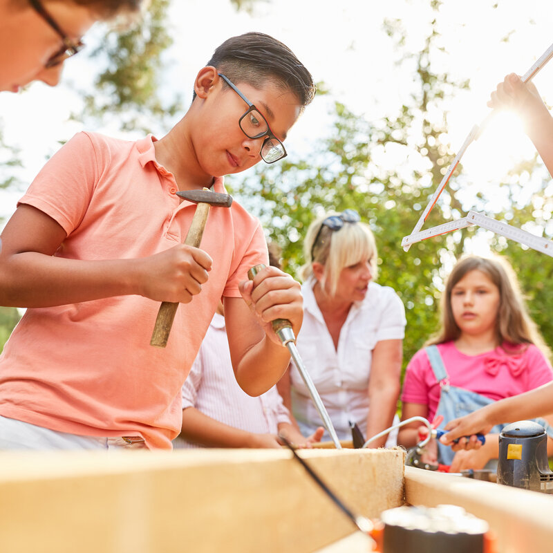 Kinder arbeiten gemeinsam draußen an einer Werkbank.