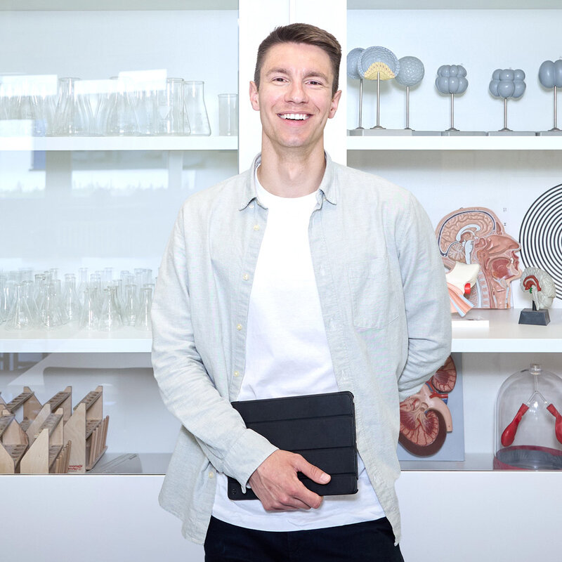 Lehrkraft Sebastian Engel steht im Biologieraum vor einer Glasvitrine und schaut in die Kamera.