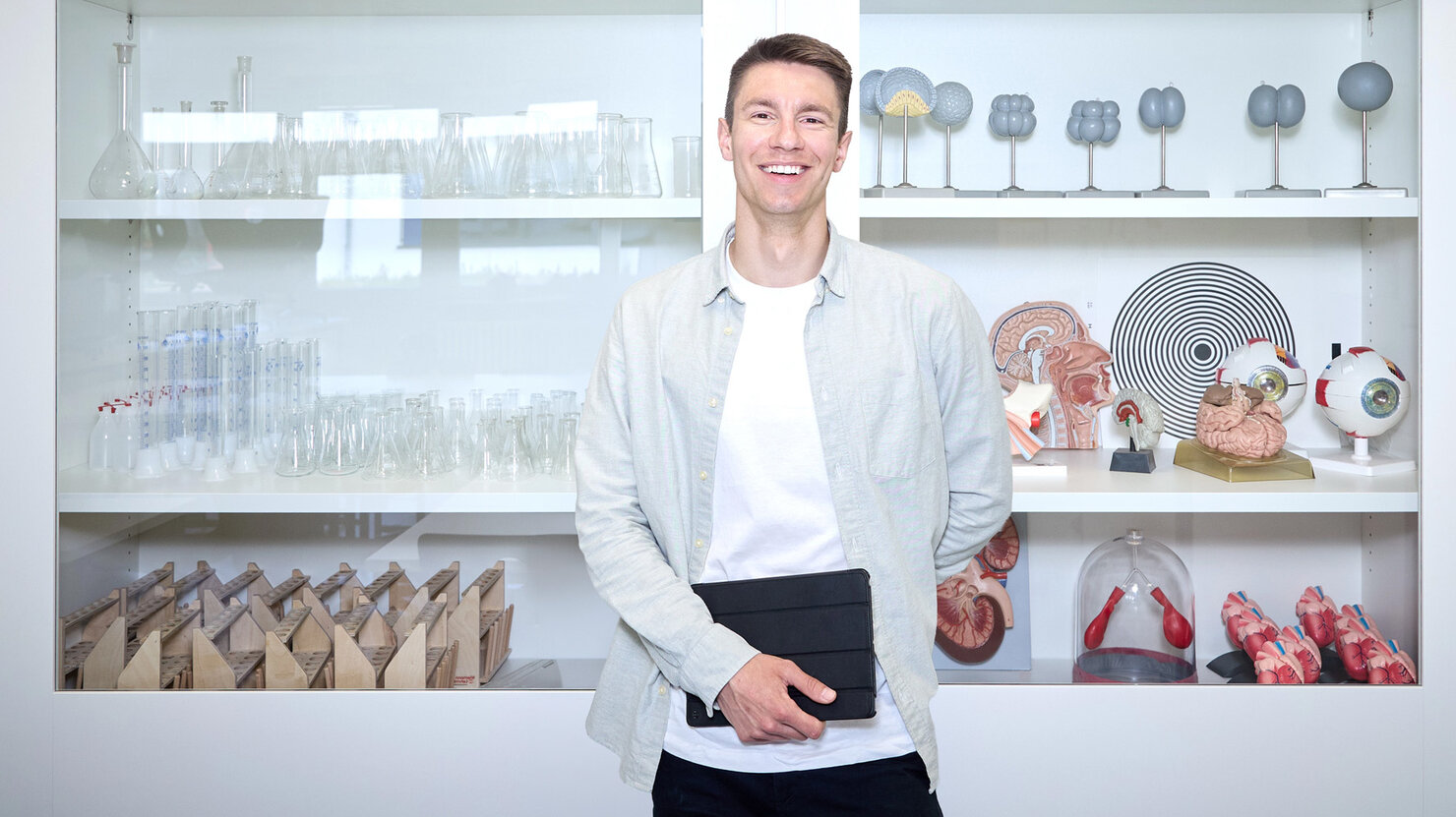 Lehrkraft Sebastian Engel steht im Biologieraum vor einer Glasvitrine und schaut in die Kamera.