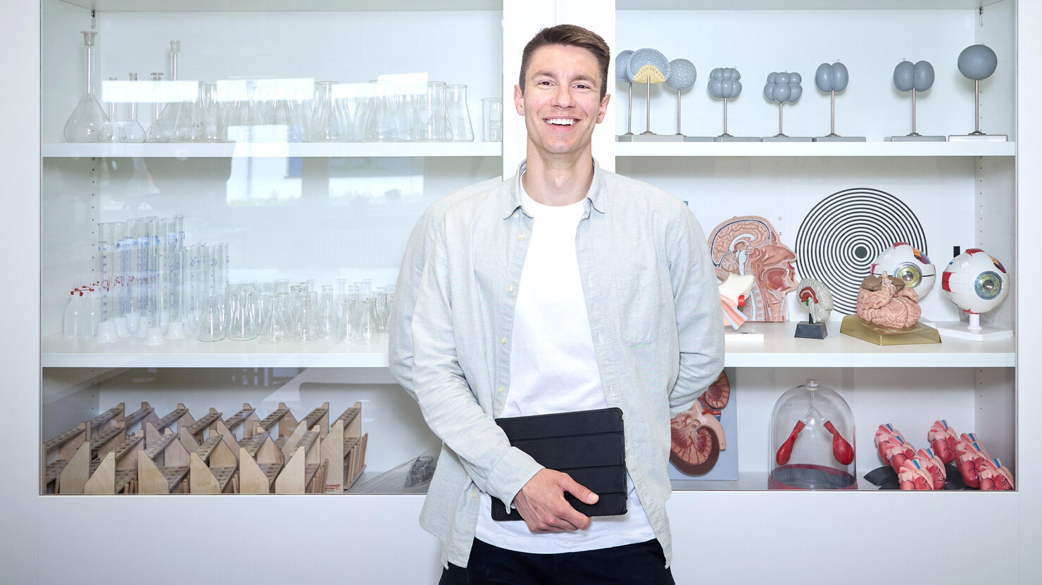 Lehrkraft Sebastian Engel steht im Biologieraum vor einer Glasvitrine und schaut in die Kamera.