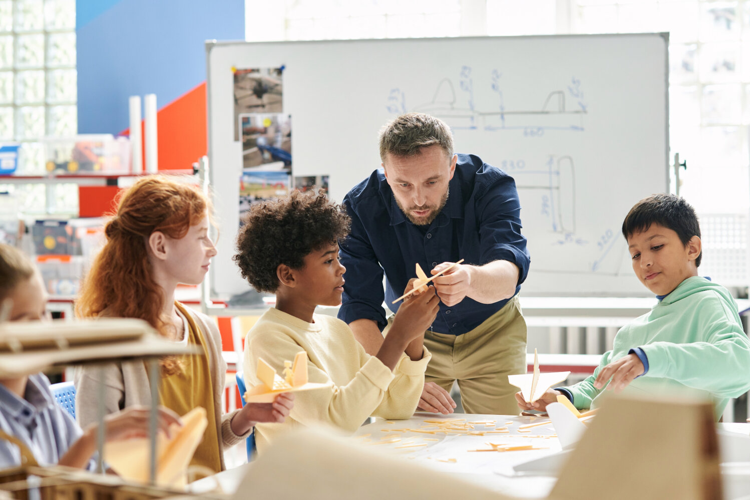 Ein Erwachsener erklärt Schüler*innen etwas.