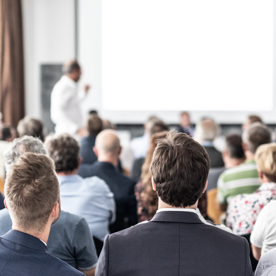 Erwachsene sitzen in einem Konferenzraum (Ansicht von hinten).