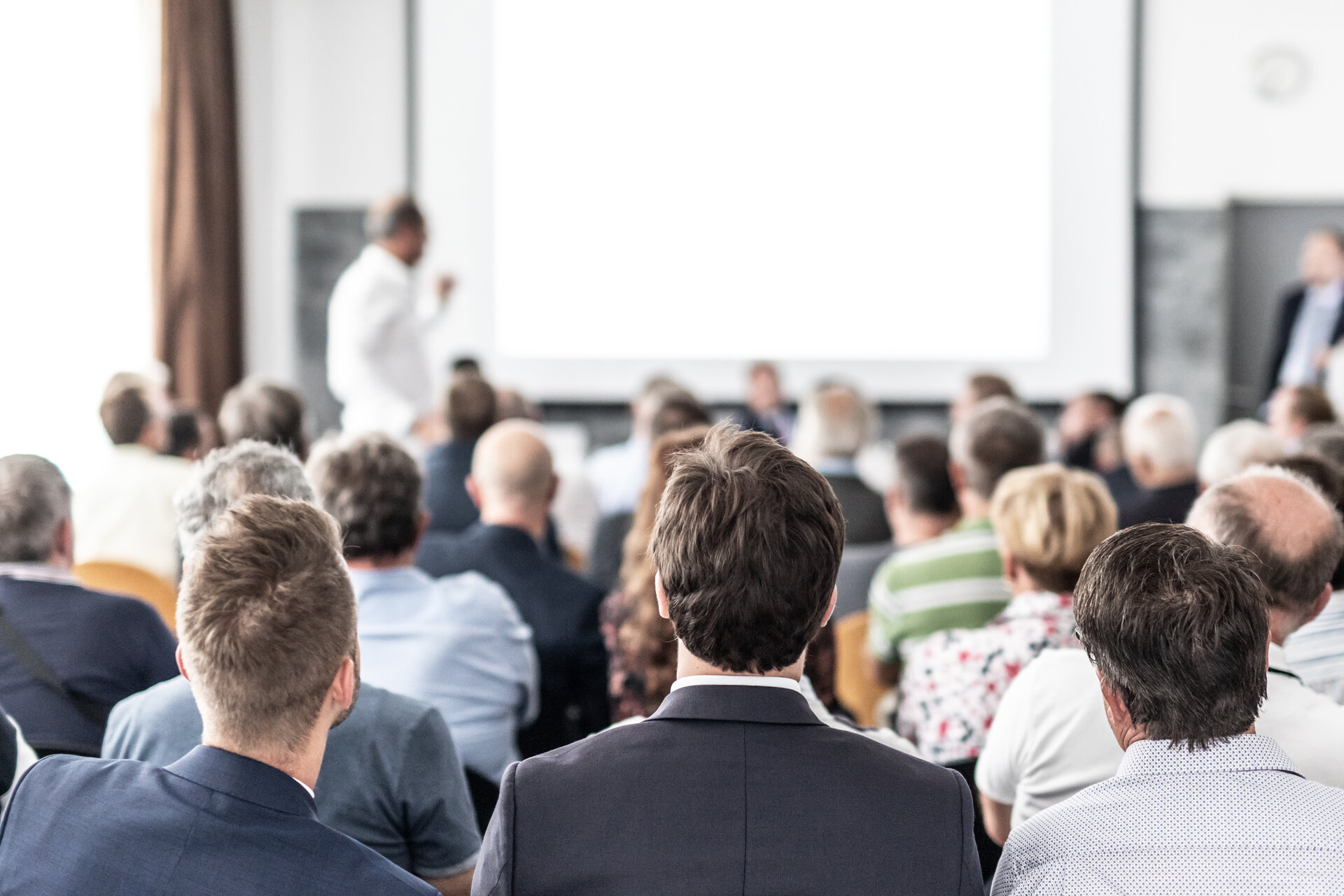 Erwachsene sitzen in einem Konferenzraum (Ansicht von hinten).