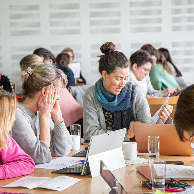 Erwachsene sitzen gemeinsam an einem großen Arbeitstisch.