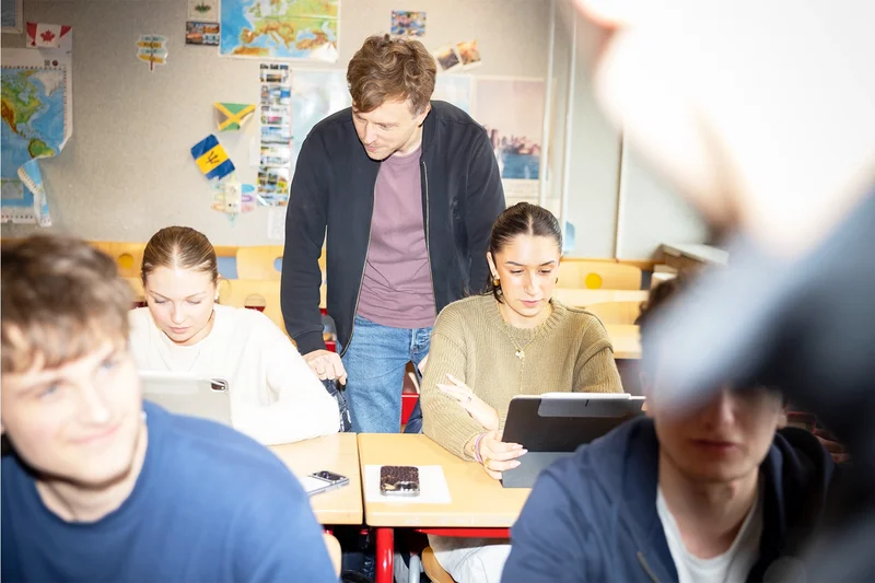 Eine Lehrkraft des Carl-Fuhlrott-Gymnasiums spricht im Klassenraum hilft zwei Schüler*innen bei einer Aufgabenstellung.