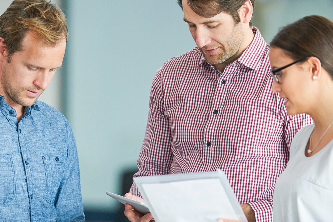 Vier Erwachsene stehen nebeneinander und schauen auf Dokumente.