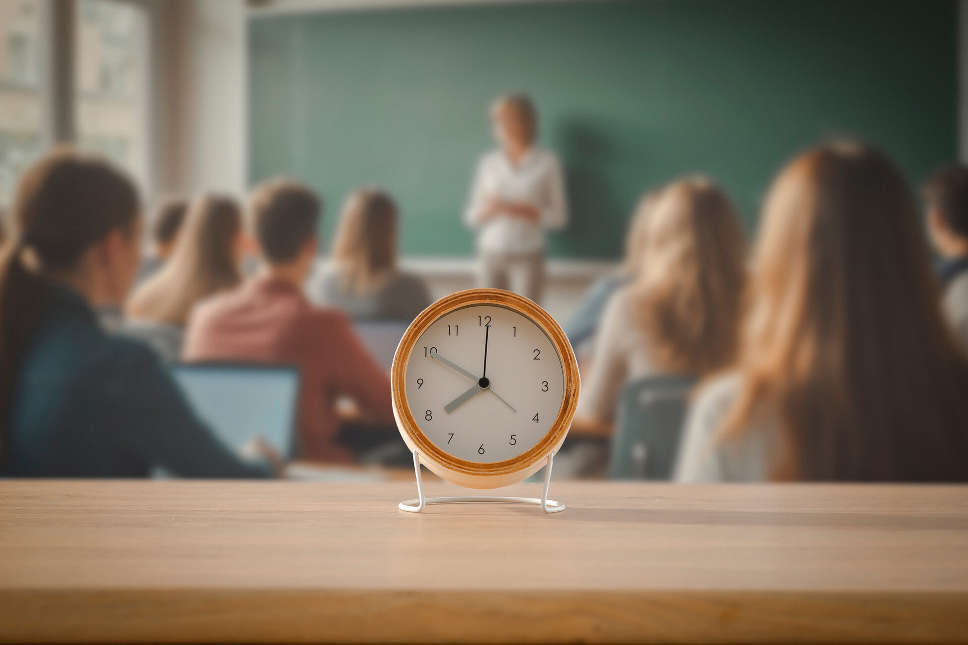 Eine Uhr ist zu sehen, im Hintergrund unscharf ein Klassenzimmer.