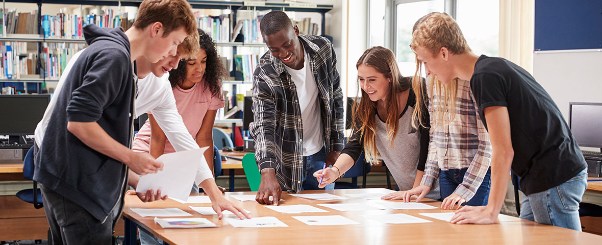 Young people stand around a table and look at documents.