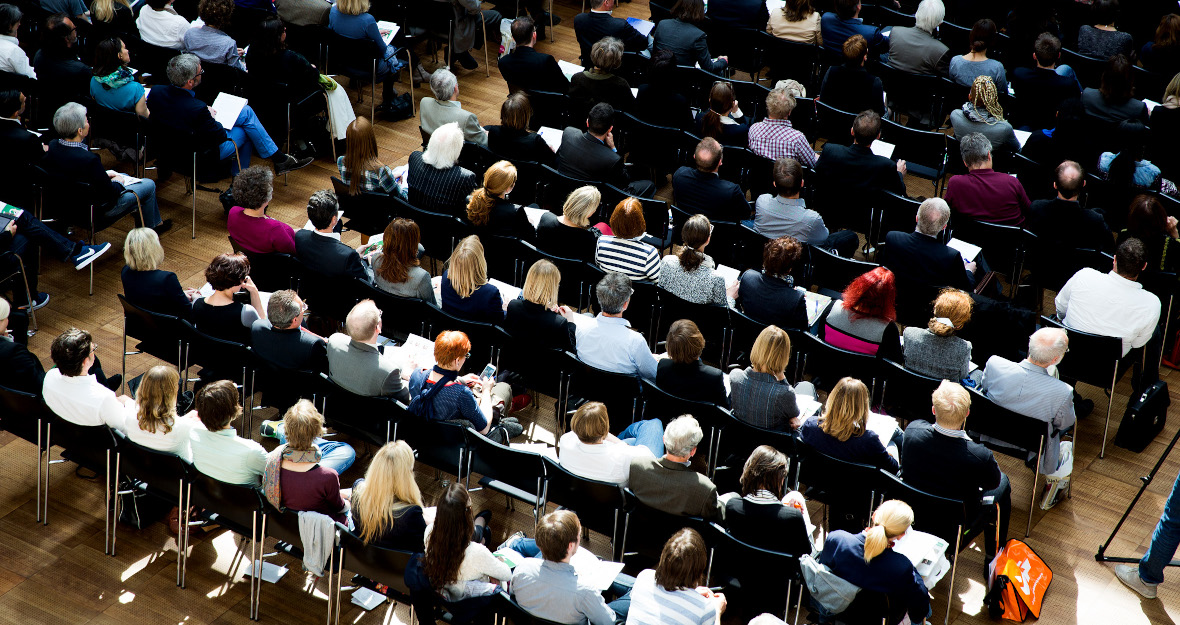 Menschen sitzen in Konferenzsaal.