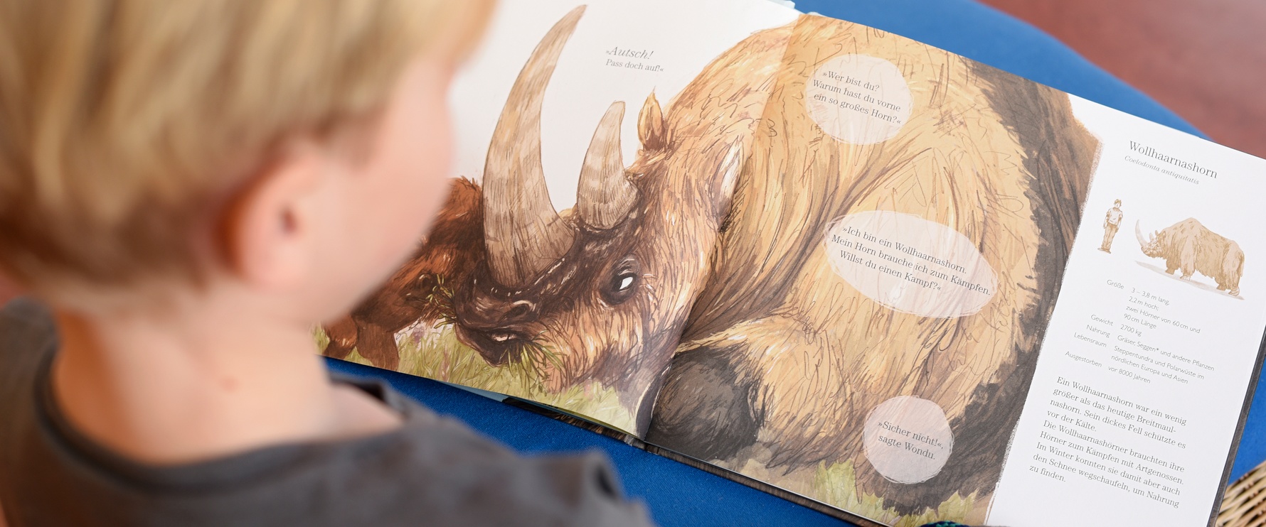 Junge schaut sich ein Buch mit einem Nashorn an