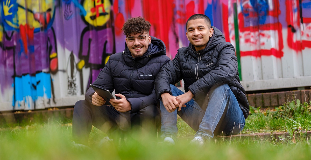 Zwei Jugendliche sitzen mit Tablet auf einer Wiese.