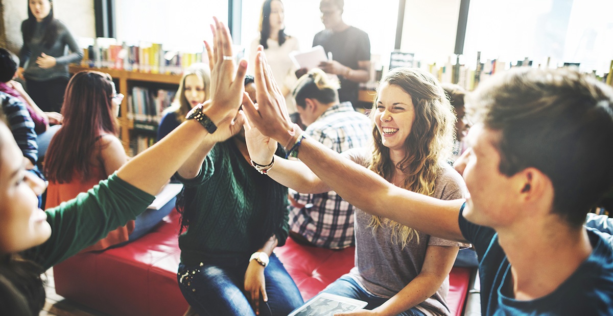 Drei Jugendliche in einer Bibliothek klatschen ein.
