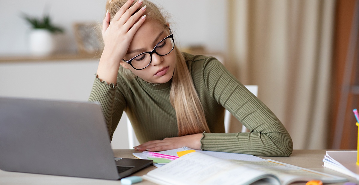 Schülerin sitzt nachdenklich am Schreibtisch vor Unterlagen und Laptop.
