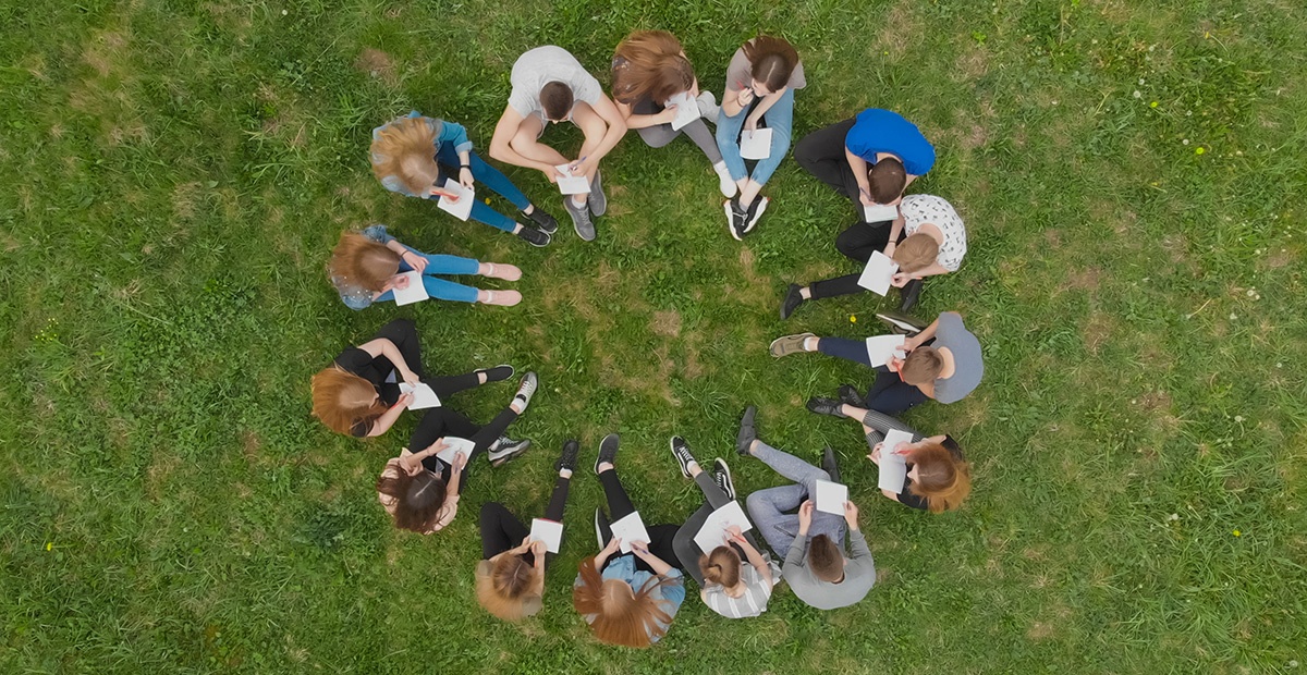 Menschen sitzen im Kreis auf einer Wiese.