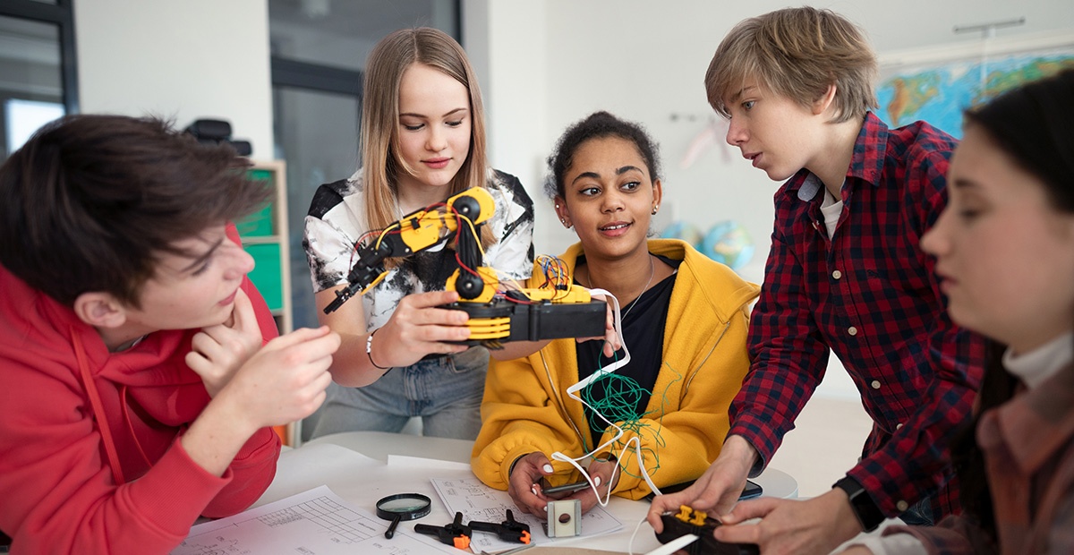 Fünf Jugendliche tüfteln gemeinsam an einem Roboterarm.