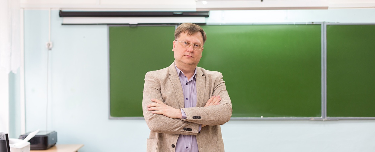 Schulleiter steht mit verschränkten Armen in Klassenzimmer.