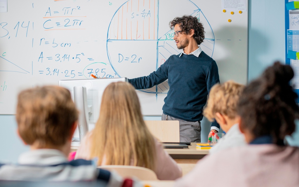 Lehrer steht vor der Klasse an der Tafel.