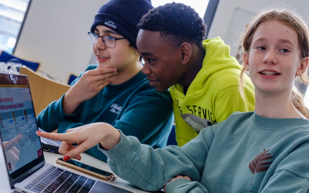 Schülerinnen und Schüler sitzen vor Laptop.