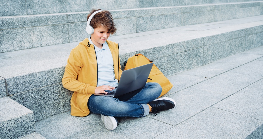 Junge sitzt mit einem Laptop auf einer Steintreppe