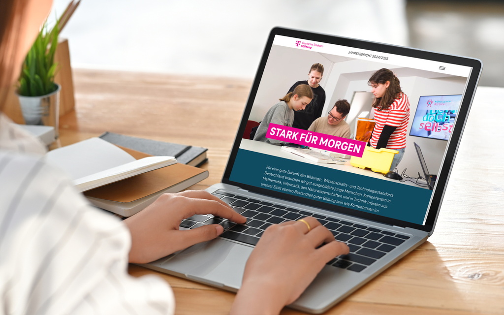 Eine Person sitzt am Schreibtisch vor einem Laptop.