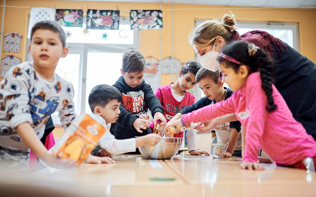 Das Bild zeigt Nina Carryer, die mit Kindern im Schulunterricht Teig anrührt.