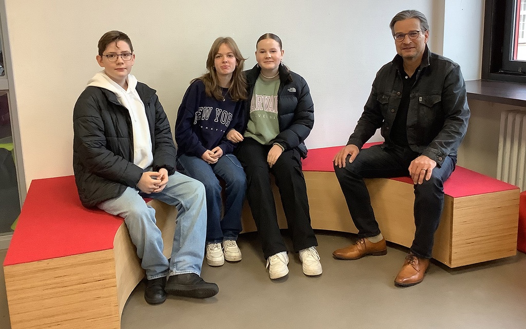 Das Foto zeigt Michael Conrads und Schüler des Ratsgymnasiums Minden, die auf einer selbstgebauten halbkreisförmigen Bank sitzen.