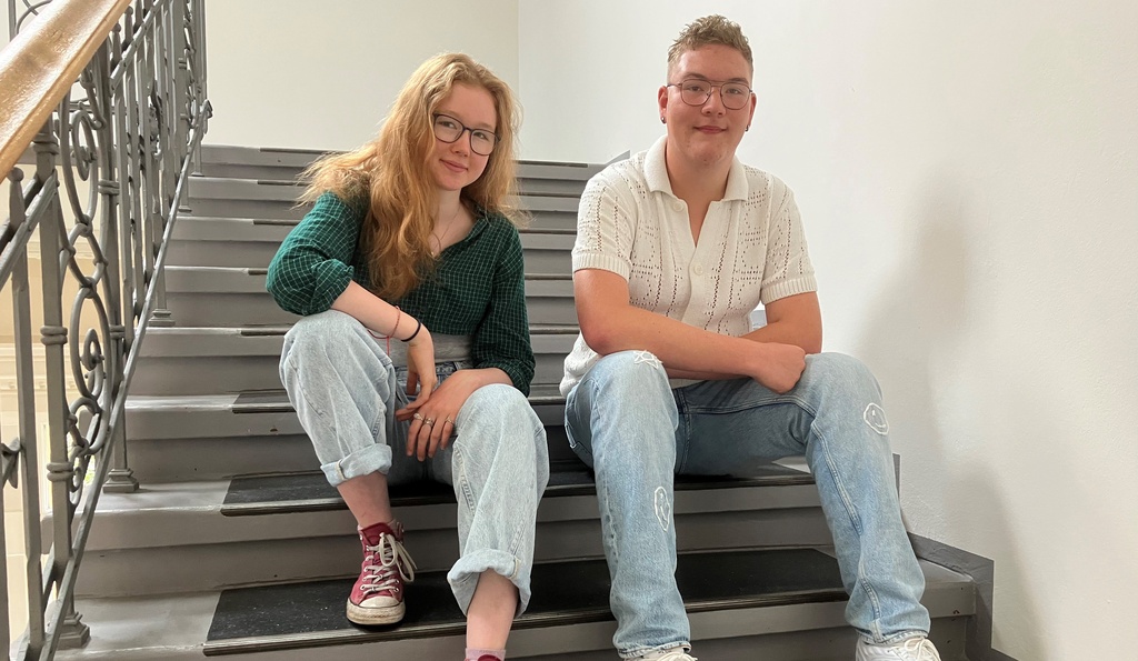 Schülerin Elli und Schüler Eddie sitzen auf einer Treppe.