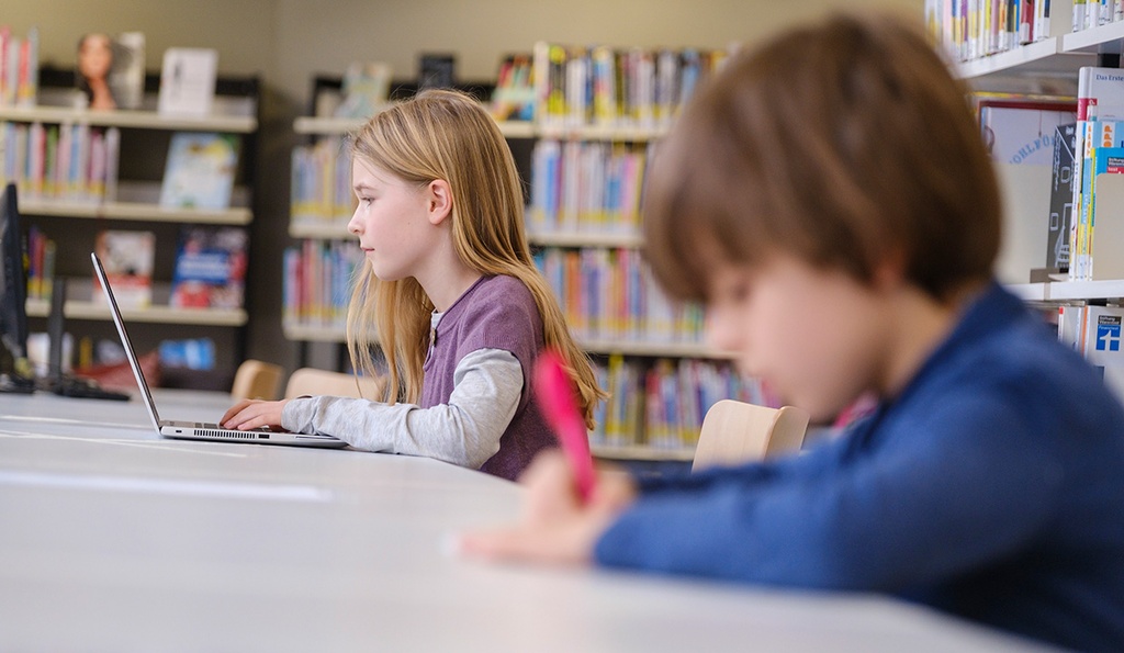 Kinder sitzen in Bibliothek.