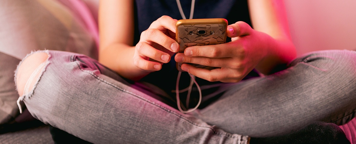 Teenager sitzt im Schneidersitz und nutzt das Smartphone