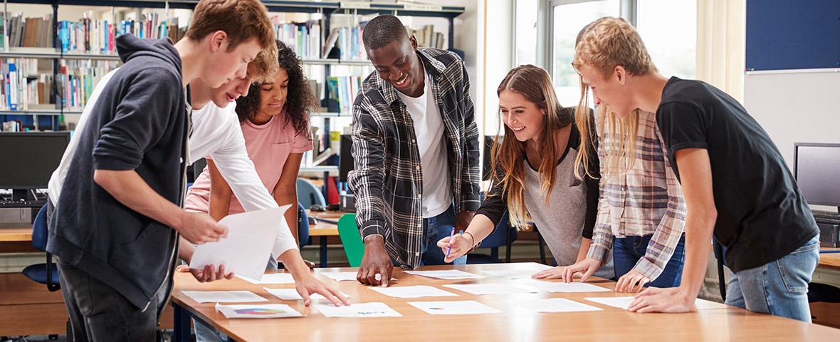 Young people stand around a table and look at documents.