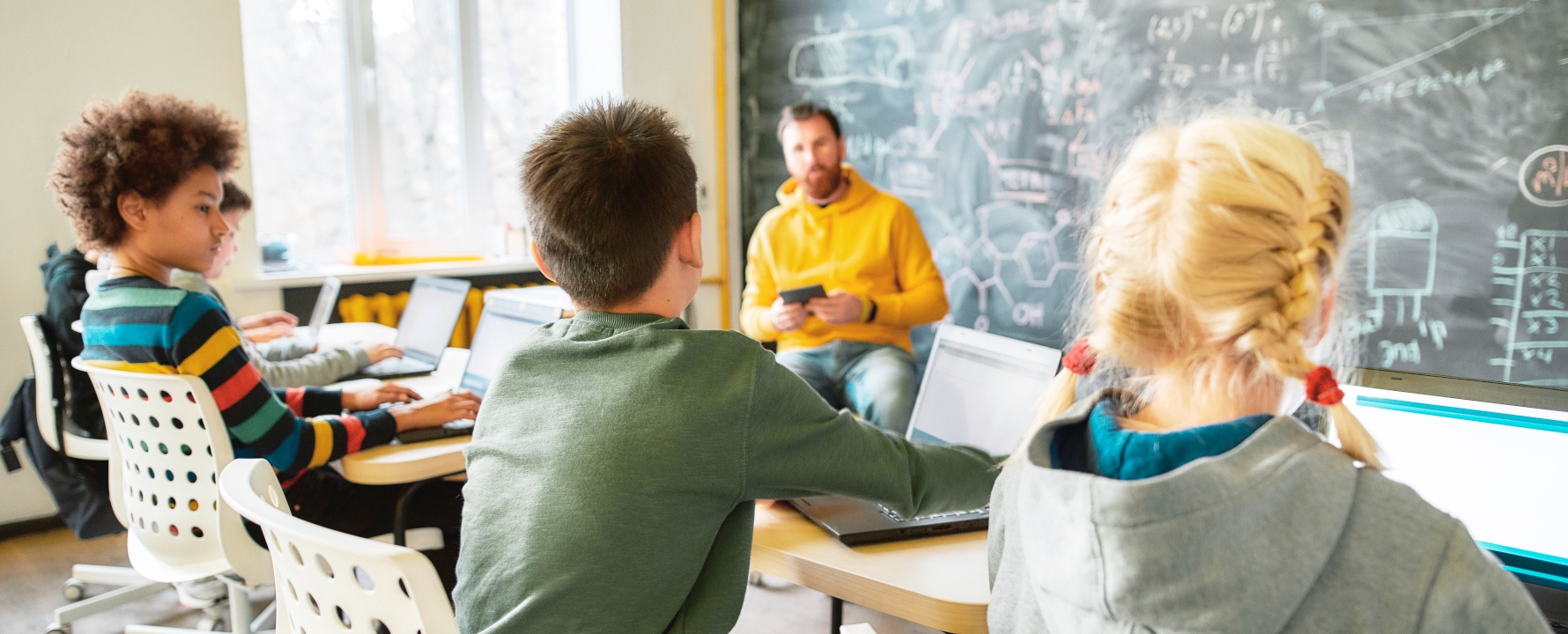 Schüler und Lehrkraft sitzen in Klassenzimmer.