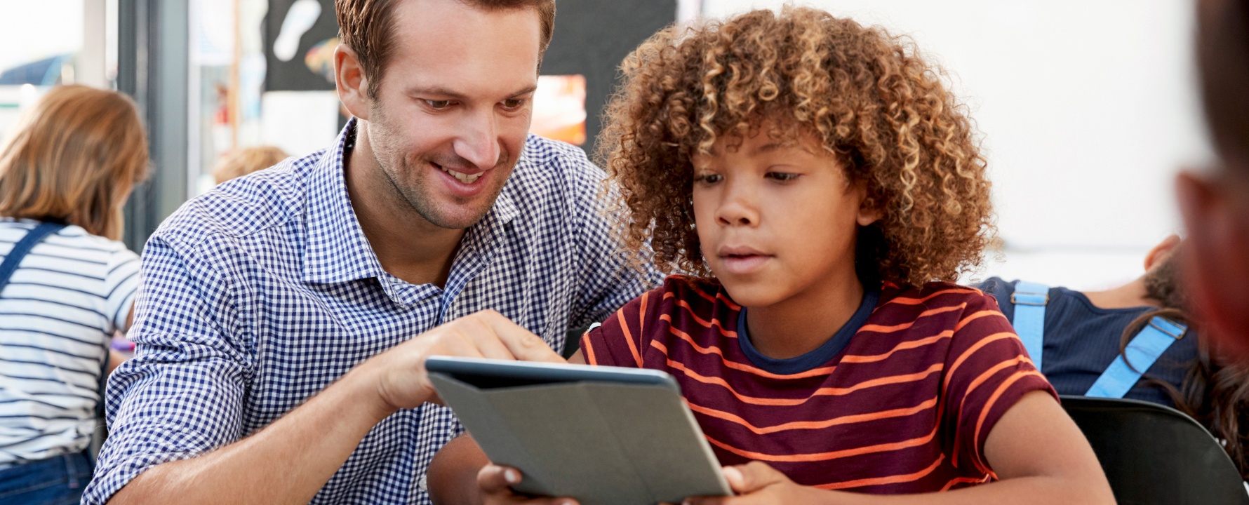 Lehrer und Schüler arbeiten gemeinsam an einem Tablet.