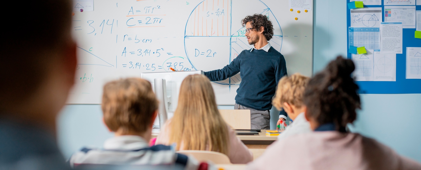Lehrer steht vor der Klasse an der Tafel.