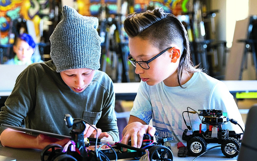 Zwei Jugendliche tüfteln an einem Roboter. 