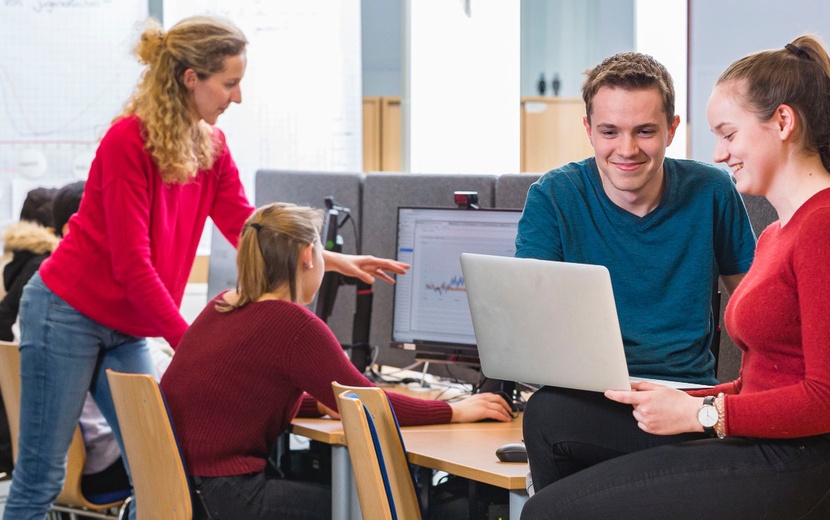 Jugendliche stehen um einen Tisch herum und betrachten Unterlagen.