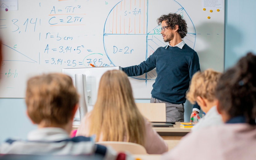 Lehrer steht vor der Klasse an der Tafel.