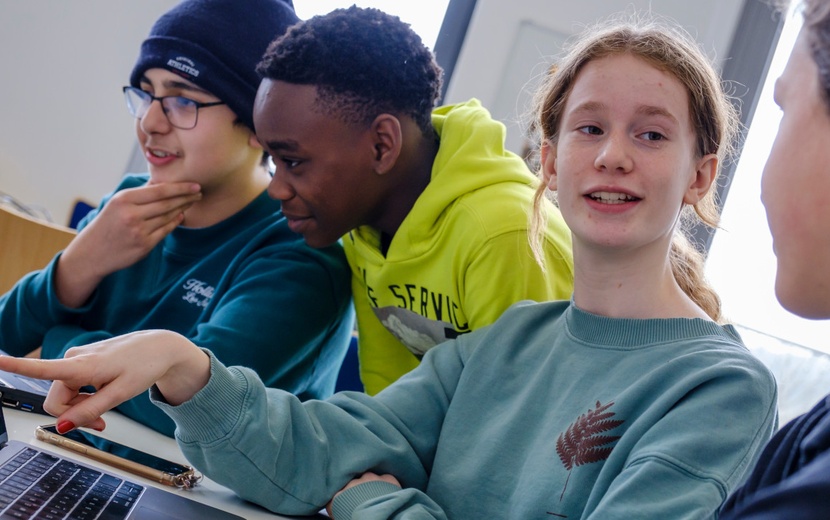 Schülerinnen und Schüler sitzen vor Laptop.