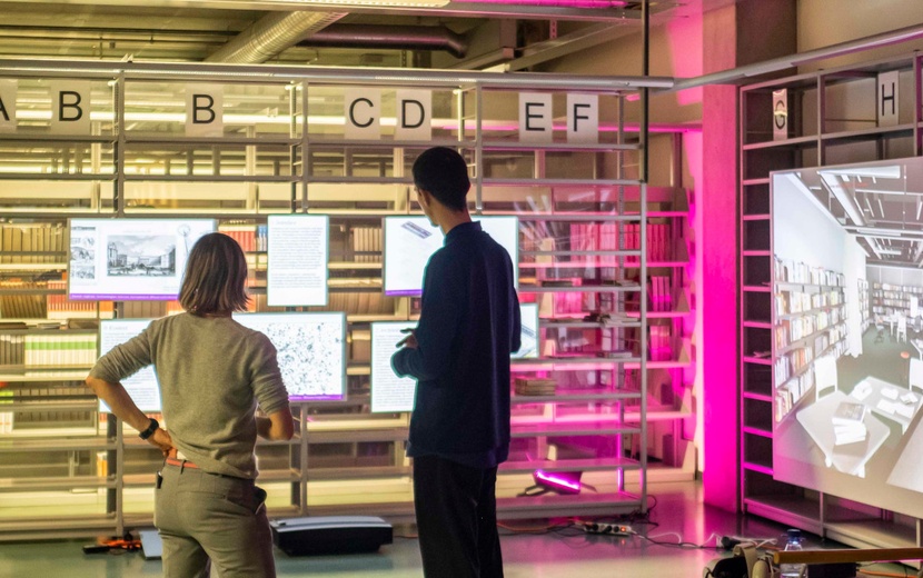 Menschen stehen in einer Bibliothek vor Info-Bildschirmen.