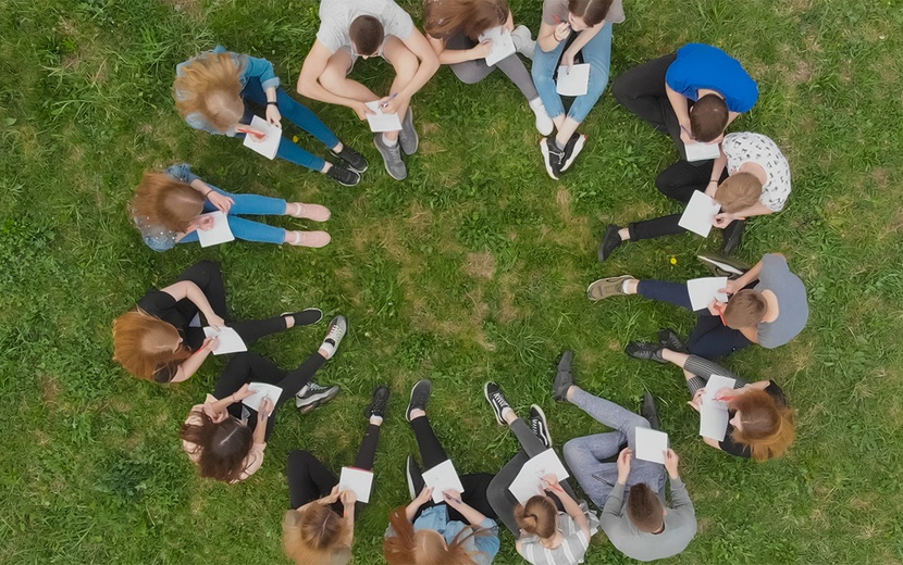 Menschen sitzen im Kreis auf einer Wiese.
