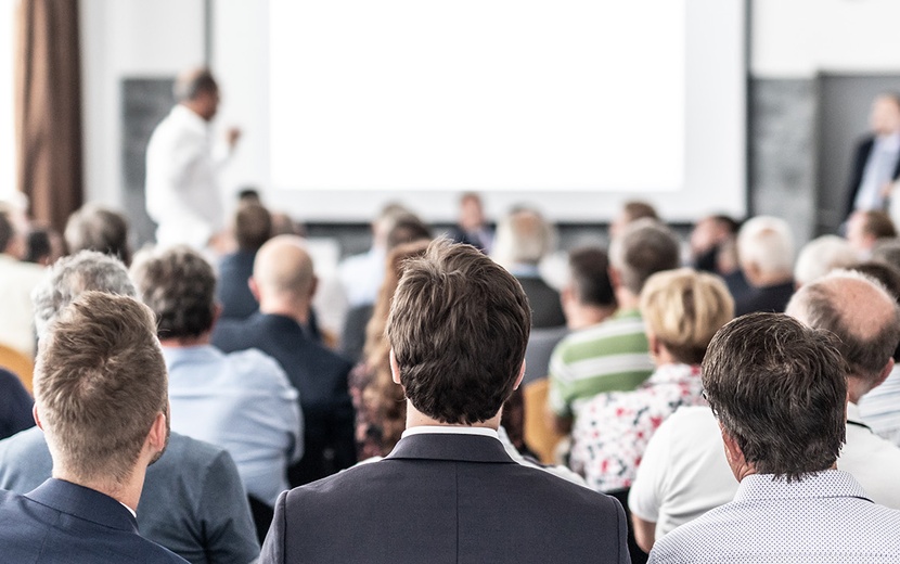 Teilnehmer in einem Konferenzraum in der Rückenansicht.